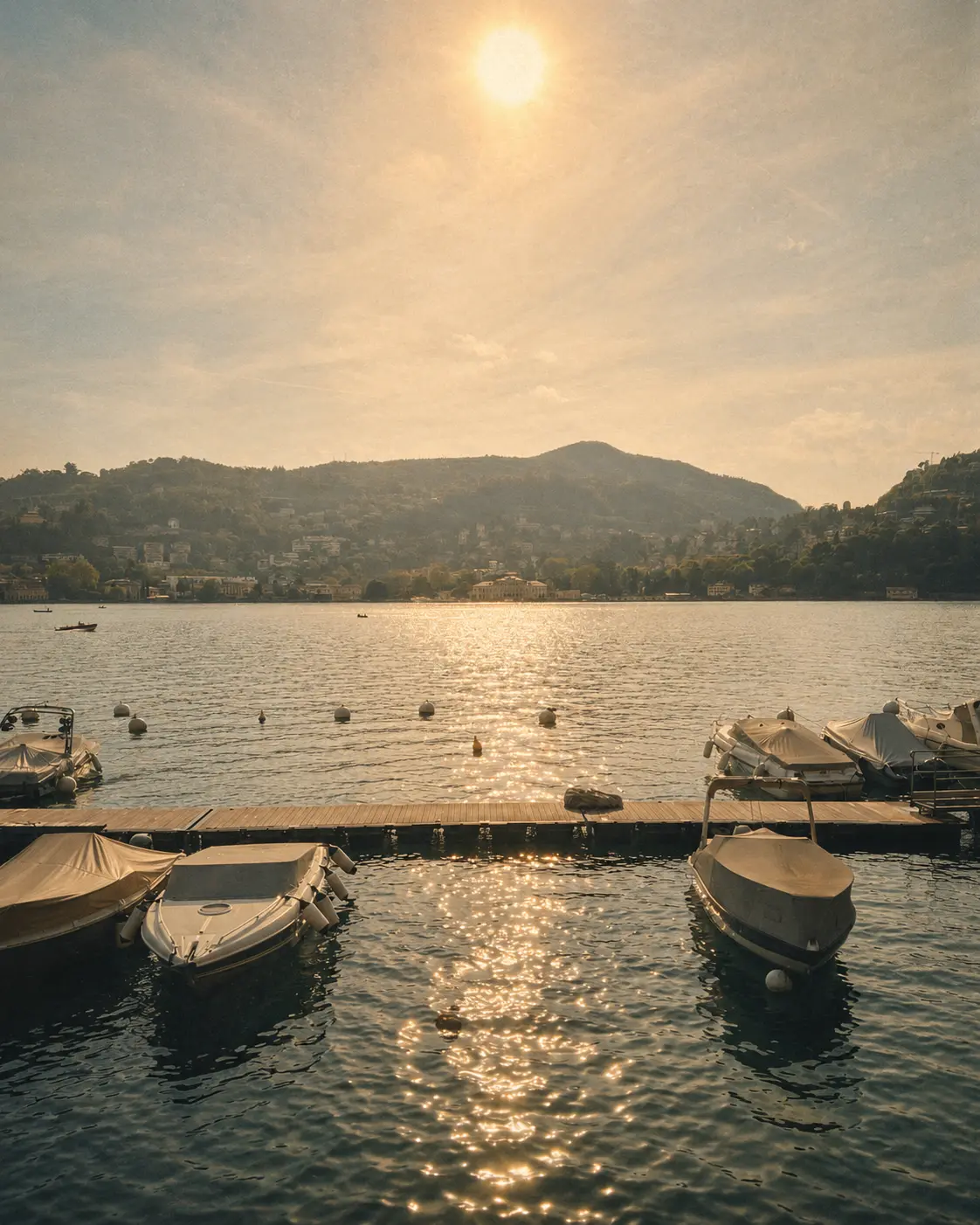 Small boats moored on calm lake water beneath a hillside in warm late-day light