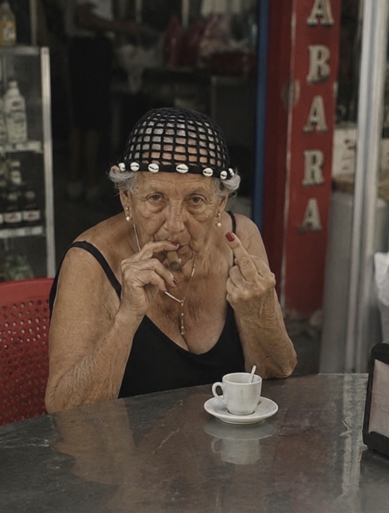 An older woman seated at an outdoor café table with an espresso