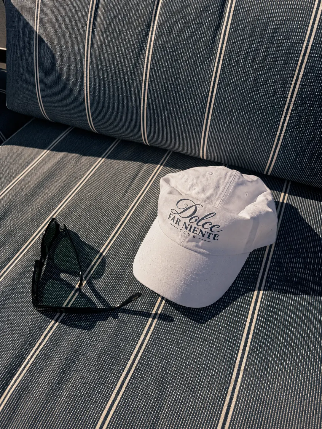 A white Dolce Far Niente Club cap and sunglasses left on a navy striped lounger