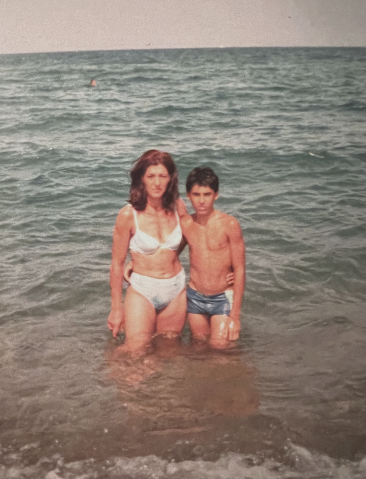 An archival photograph of a mother and child standing in shallow sea water