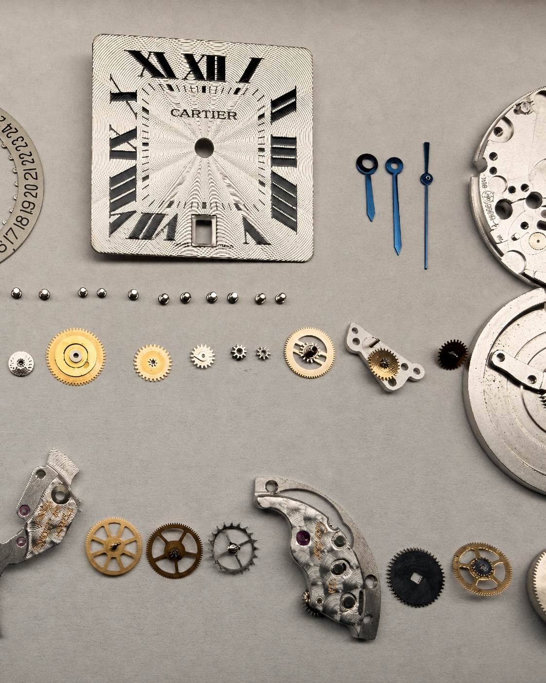 The dial, hands, wheels and bridges of a Cartier watch laid out in rows before assembly