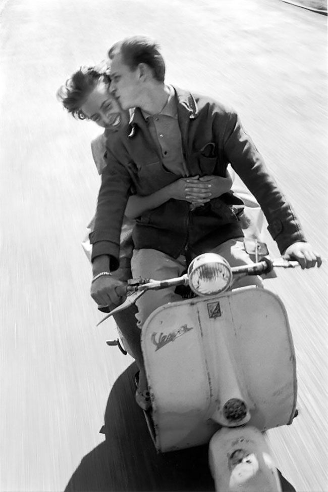 A black and white photograph of a couple riding together on a Vespa