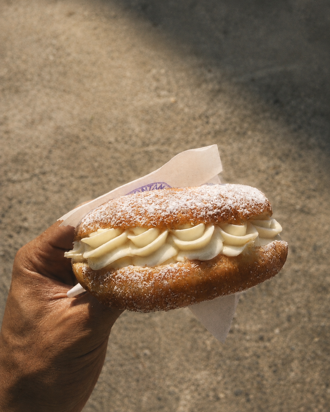 A hand holding a cream-filled brioche dusted with sugar