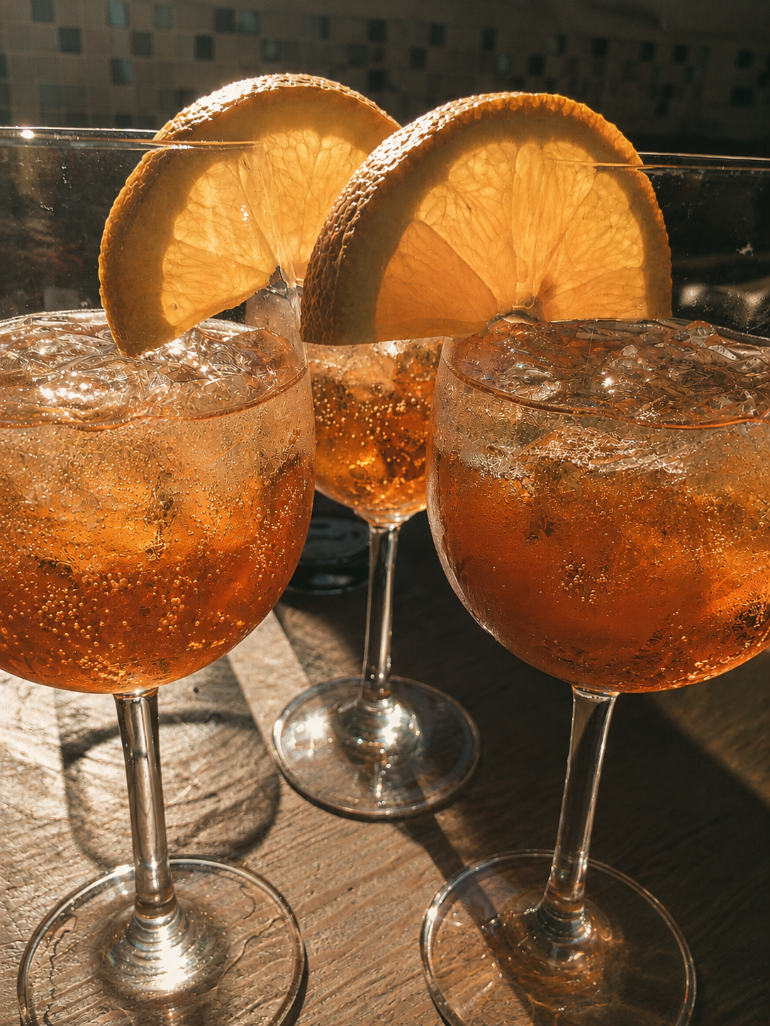 Three spritzes with orange slices on a wooden table in low sun