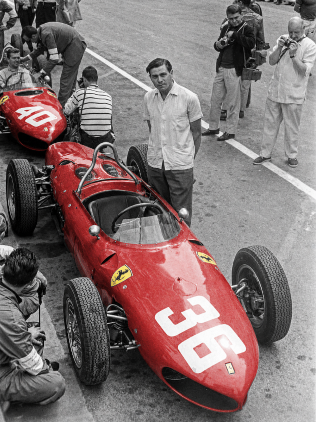 Vintage red Ferrari Formula 1 cars numbered 36 and 40 in a pit lane, with Prancing Horse badges and mechanics in attendance